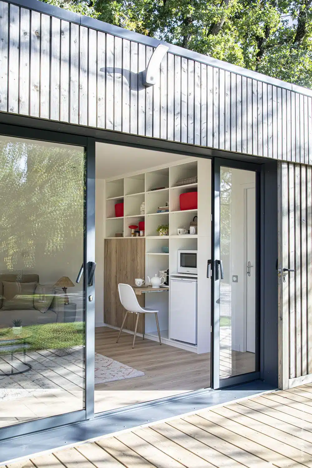 Intérieur compact visible depuis des portes vitrées ouvertes, avec kitchenette et espace assis